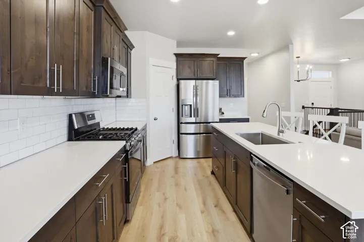 Kitchen featuring dark wood cabinetry, white quartz countertops, subway tile backsplash, stainless steel appliances, and wood-finish flooring