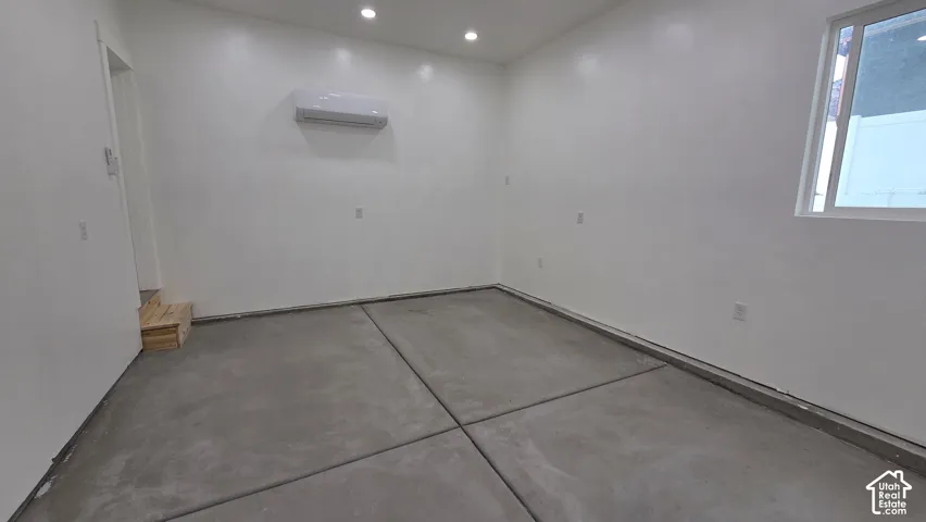 Interior space featuring smooth concrete flooring, recessed lighting, white walls, and a wall-mounted climate control unit
