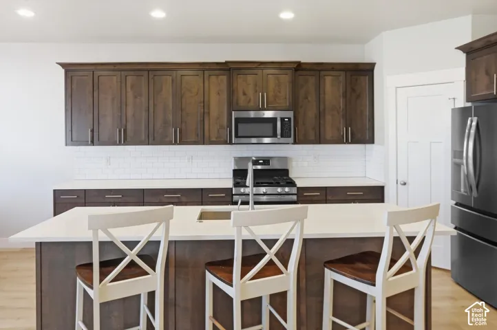 Kitchen featuring wood cabinetry, a central island with a solid surface countertop, white subway tile backsplash, and stainless steel appliances