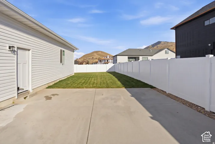 Concrete patio area with a fenced backyard, featuring horizontal siding, a white vinyl privacy fence, and mountain backdrop
