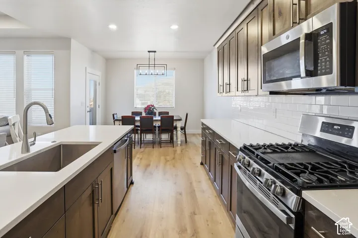 Kitchen featuring wood-finish cabinetry, quartz countertops, a white subway tile backsplash, stainless steel appliances, and wood-finish flooring