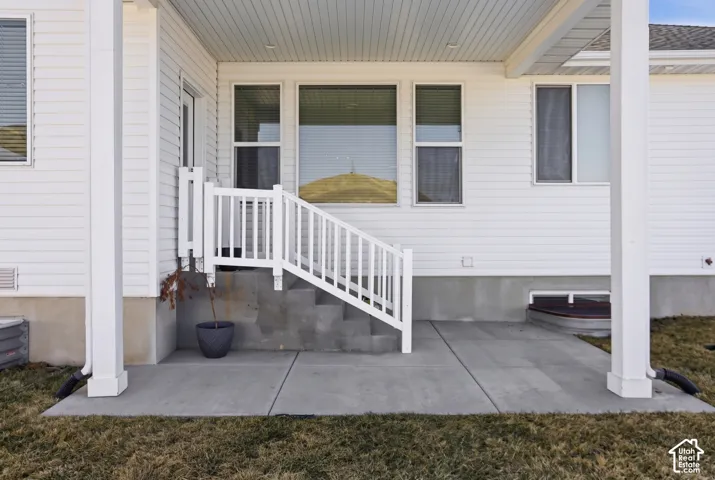 Covered concrete patio featuring white siding, a concrete staircase with white railings, and an egress window well