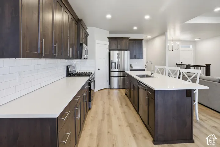 Kitchen featuring dark-finish cabinetry, light-toned countertops, white subway tile backsplash, stainless steel appliances, and wood-finish flooring