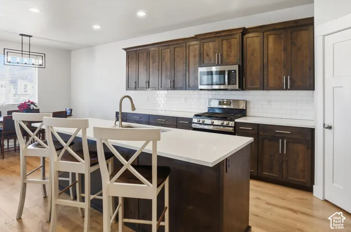 Kitchen featuring wood-finish cabinetry, white solid-surface countertops, subway tile backsplash, stainless steel appliances, and wood-finish flooring