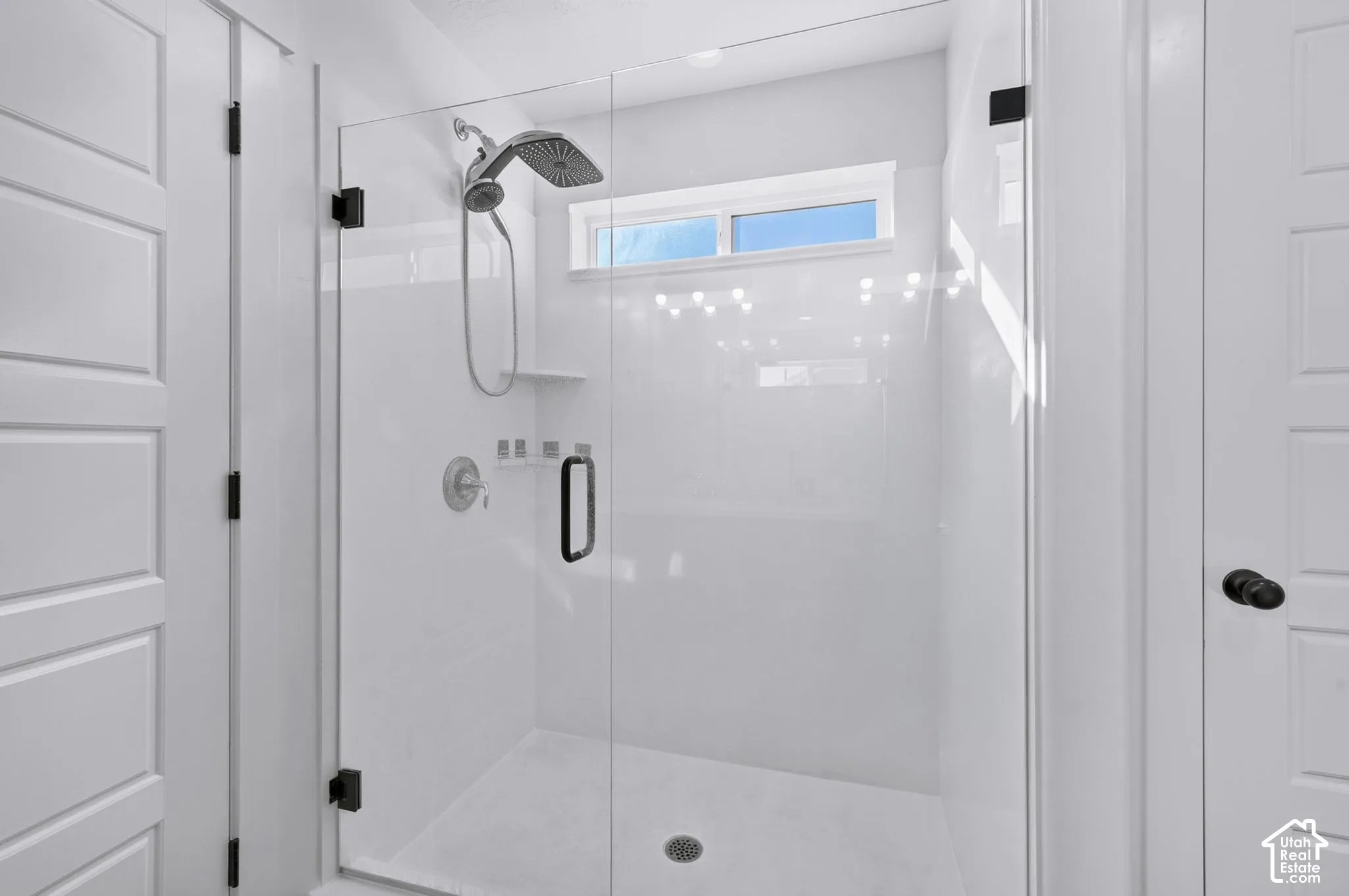 Walk-in shower featuring a frameless glass door, solid-surface surround, rain-style showerhead with handheld sprayer, built-in shelving, and black finish hardware