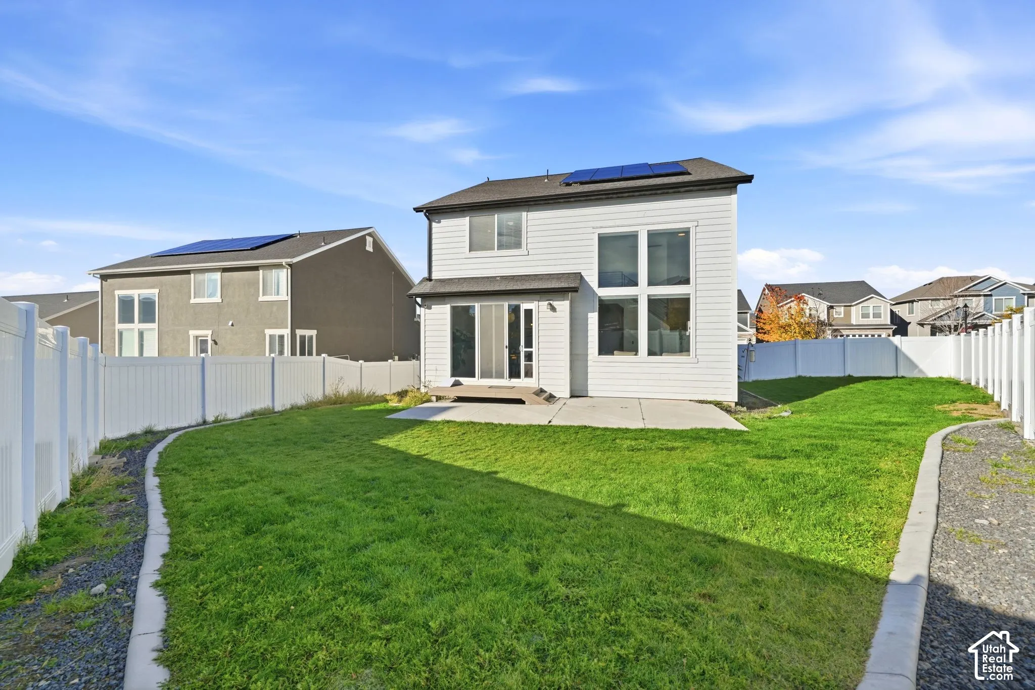Rear exterior featuring horizontal siding, expansive windows, rooftop solar panels, a concrete patio, and a fenced backyard with lawn