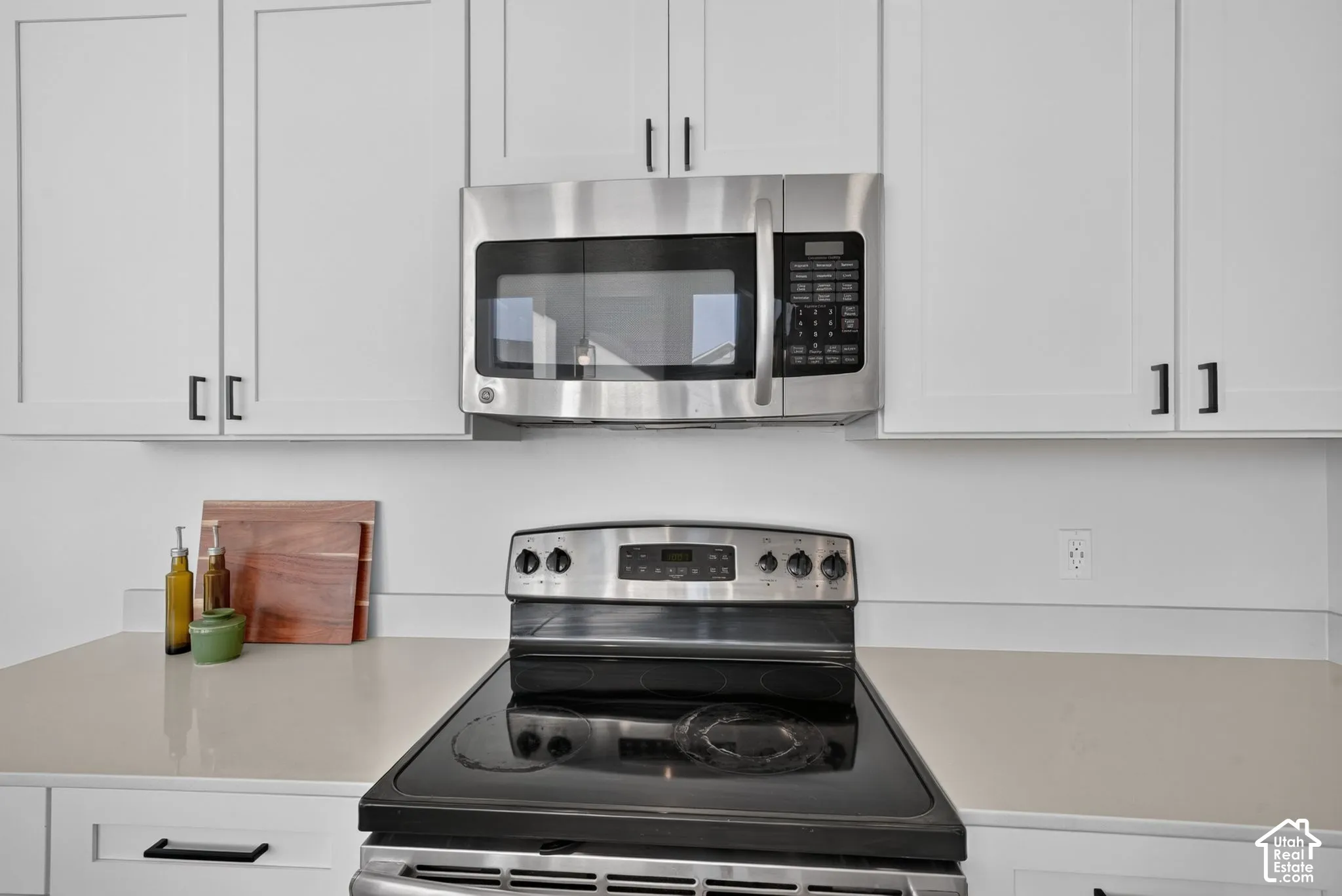 Shaker-style white cabinetry with matte black hardware, stainless steel over-the-range microwave, smooth-top electric range, and solid-surface countertop