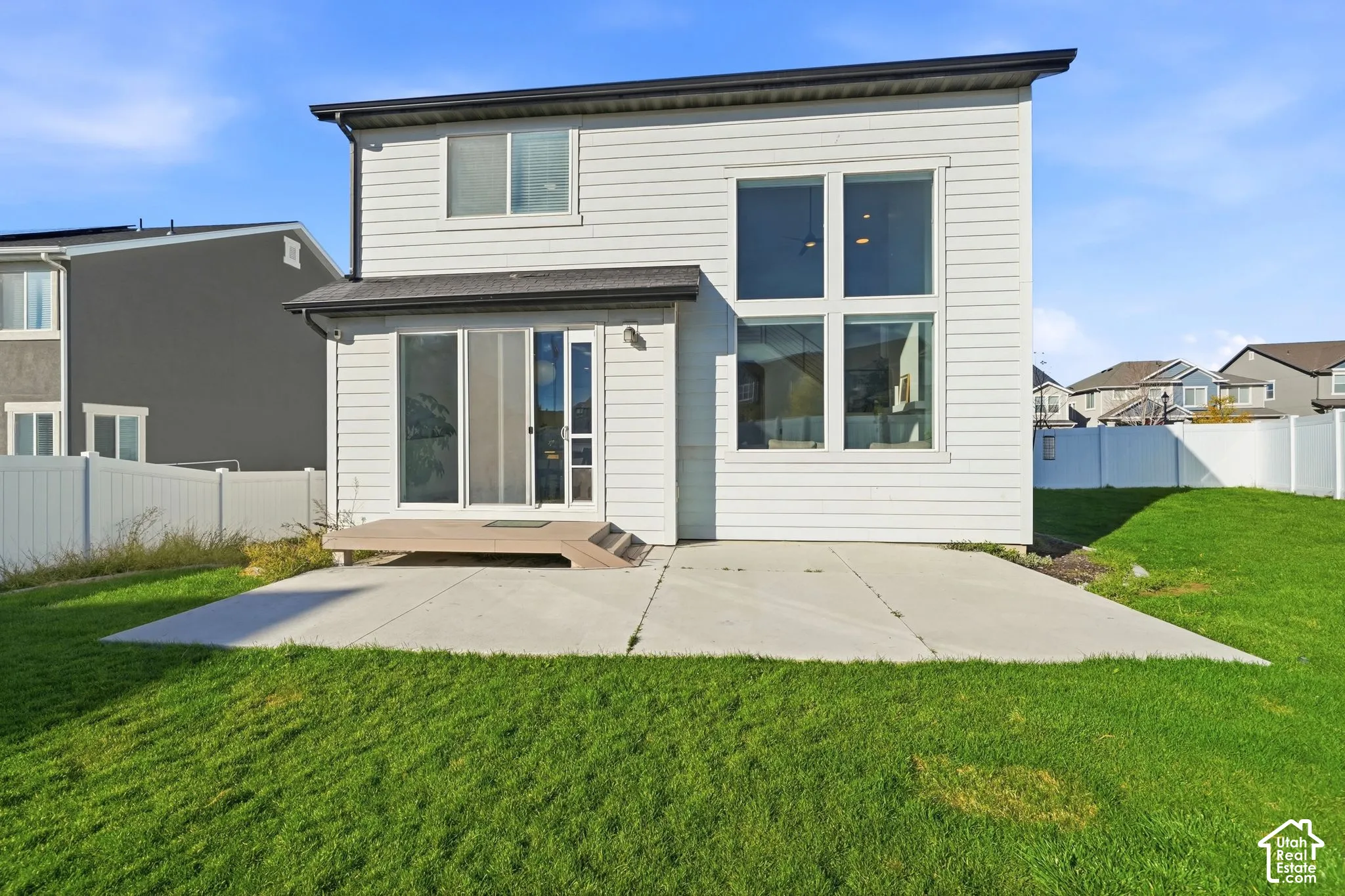 Rear exterior featuring horizontal lap siding, large dual-pane windows, a concrete patio, a composite deck, and white vinyl perimeter fencing