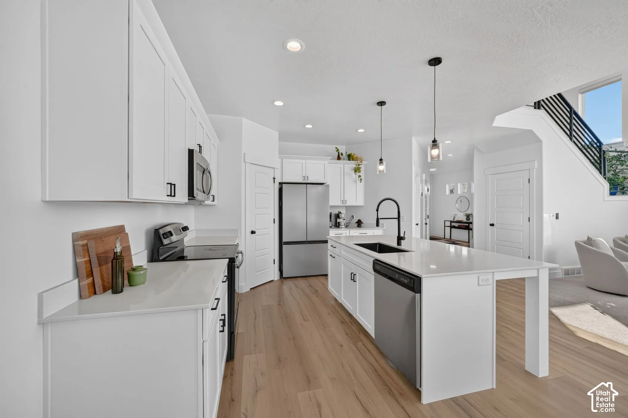 Kitchen featuring white cabinetry, quartz countertops, a central island with a matte black faucet, stainless steel appliances, and wood-finish flooring