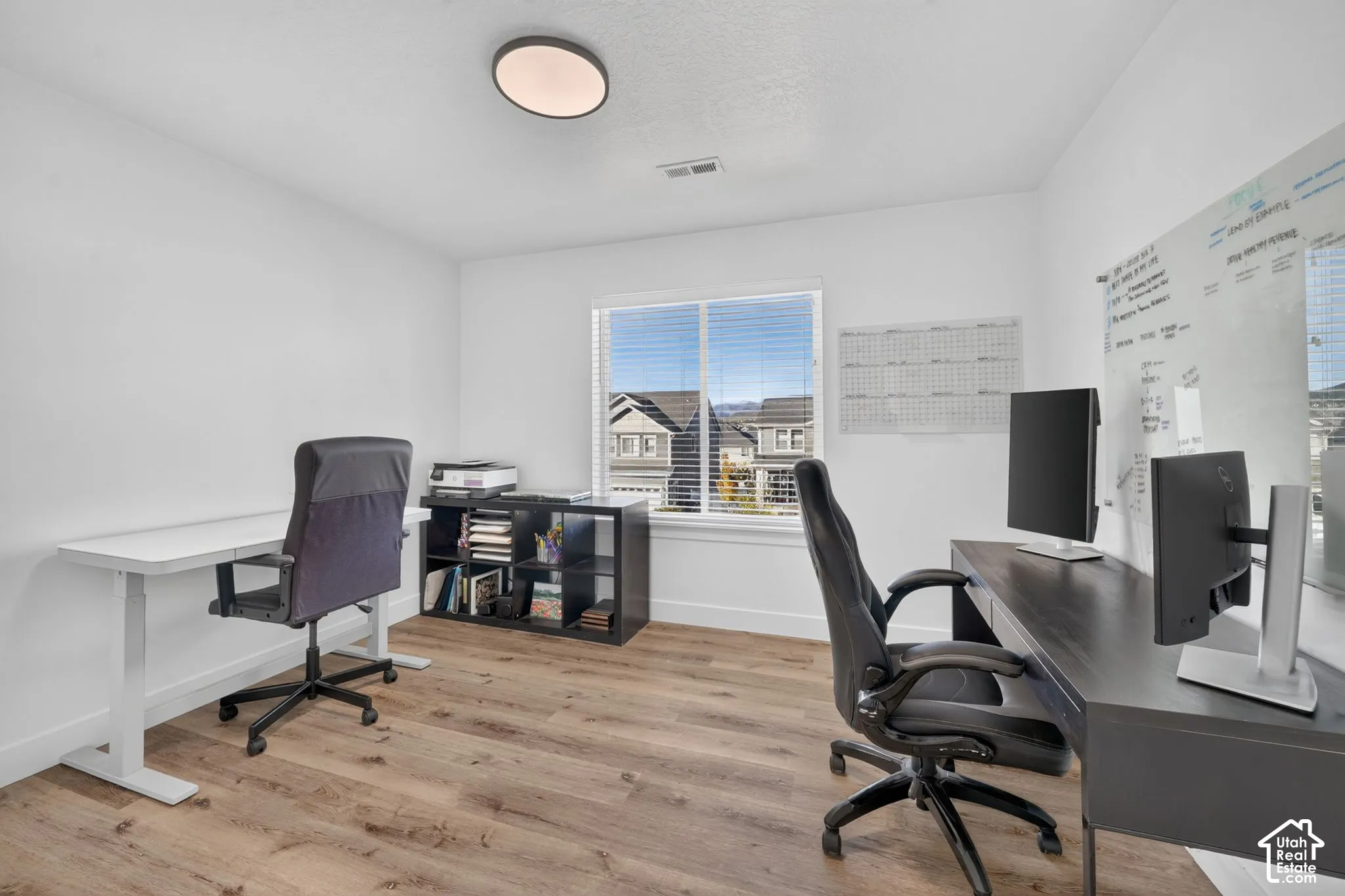 Room featuring wood-finish flooring, a large window with horizontal blinds, and a circular flush-mount ceiling light