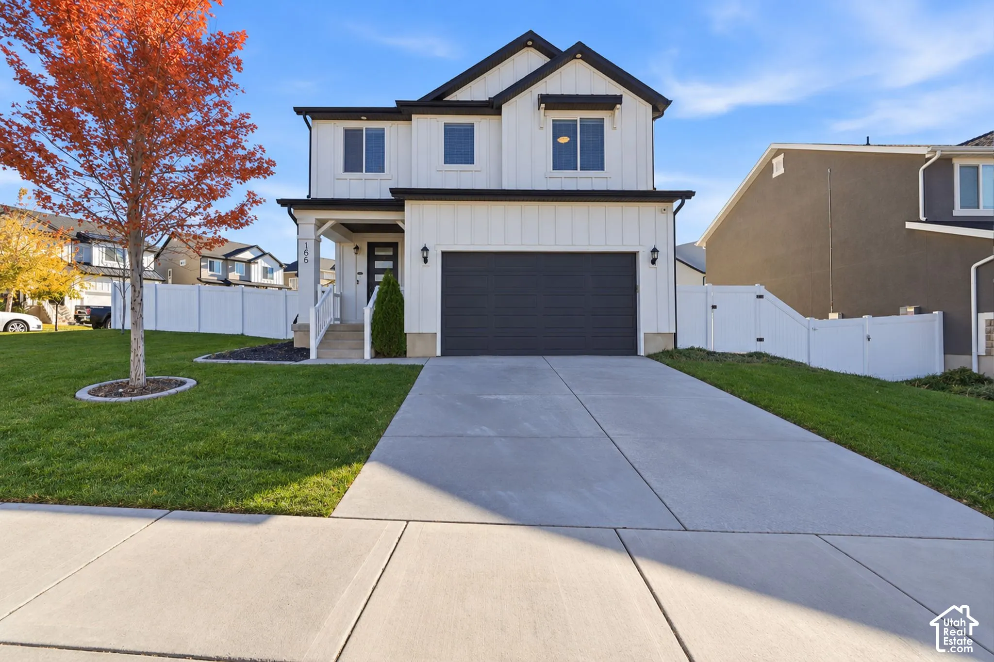 Two-story residence featuring white vertical siding, a front-facing attached garage, a covered entryway, and white perimeter fencing