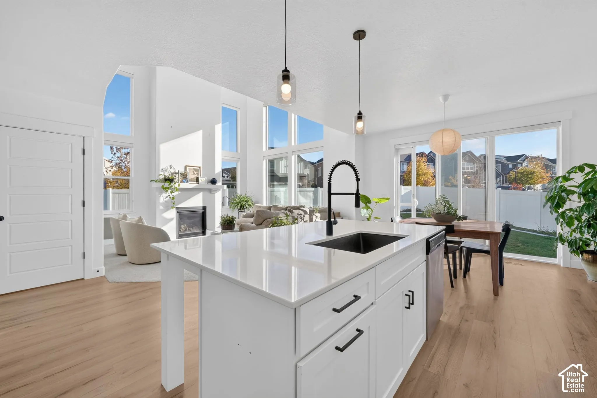 Kitchen island with a quartz countertop, under-mount sink, and matte black faucet, complemented by wood-finish flooring, floor-to-ceiling windows, and a built-in fireplace