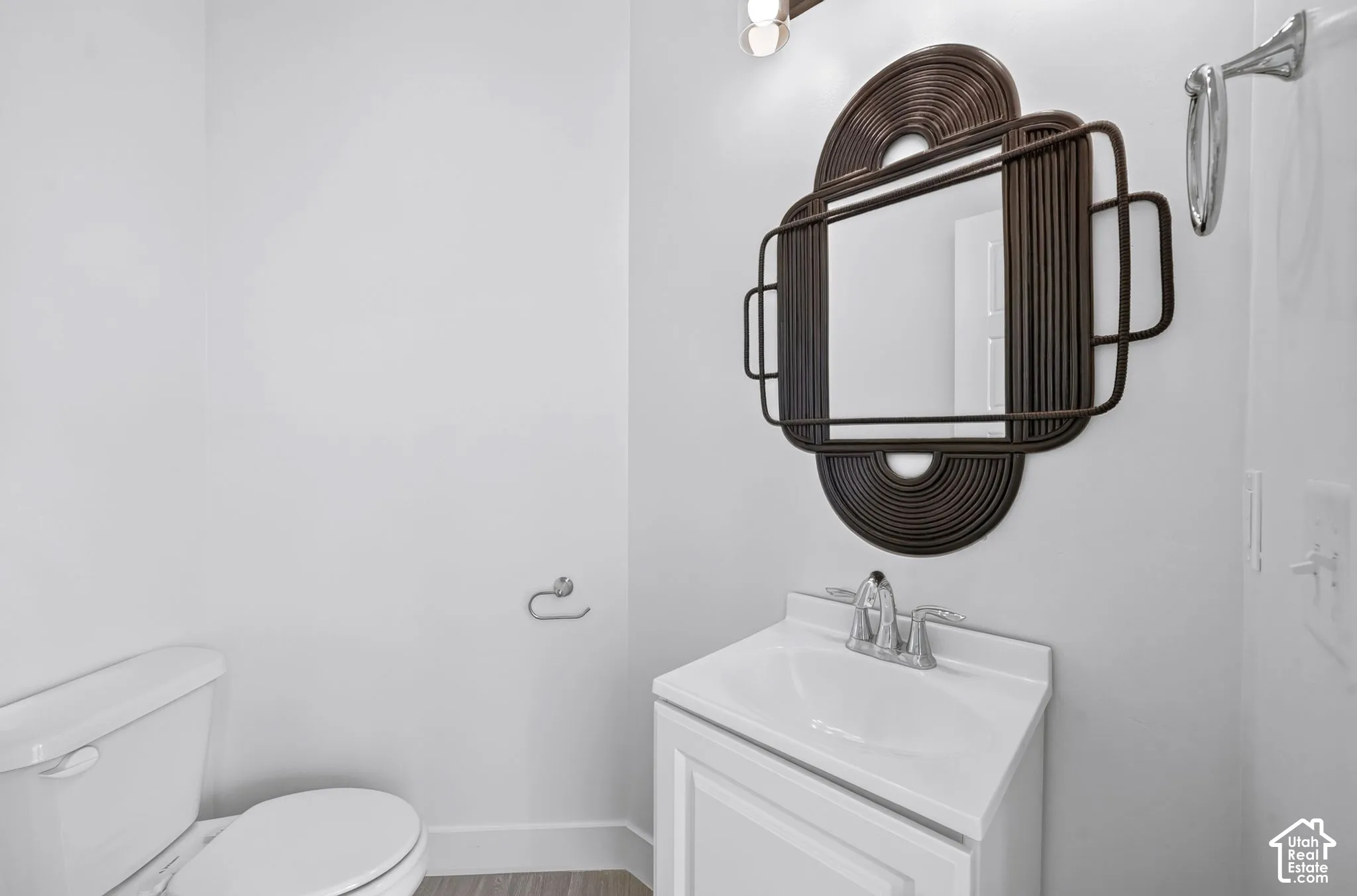 White vanity cabinet with an integrated sink and polished chrome faucet, paired with a decorative dark-finish wall-mounted mirror, overhead vanity lighting, and chrome hardware