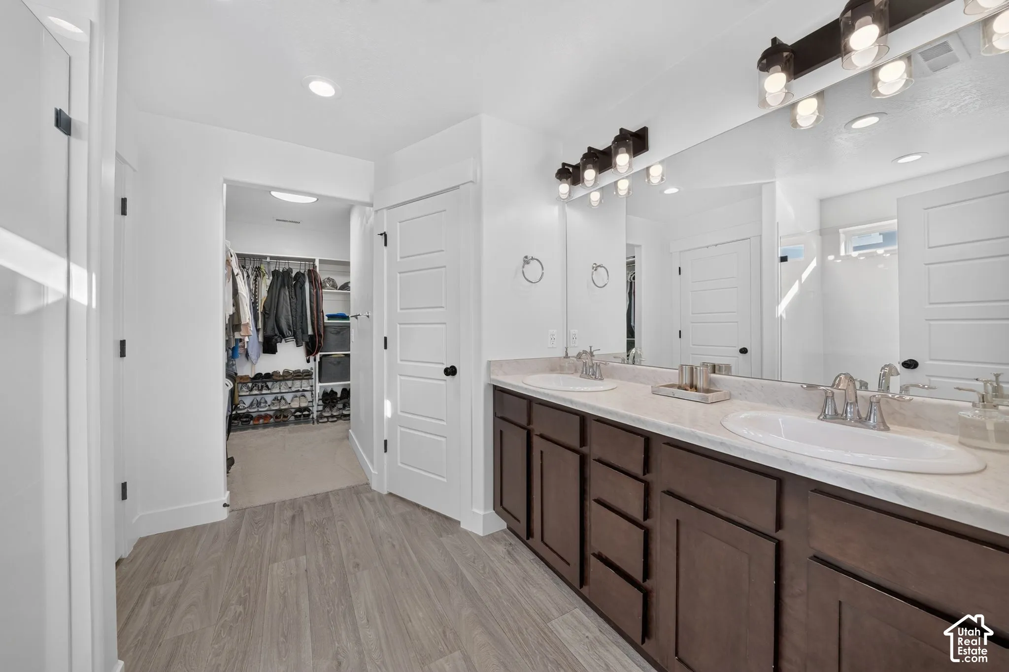 Double vanity featuring dark wood cabinetry, solid surface countertops, dual undermount sinks, and wall-mounted industrial-style lighting