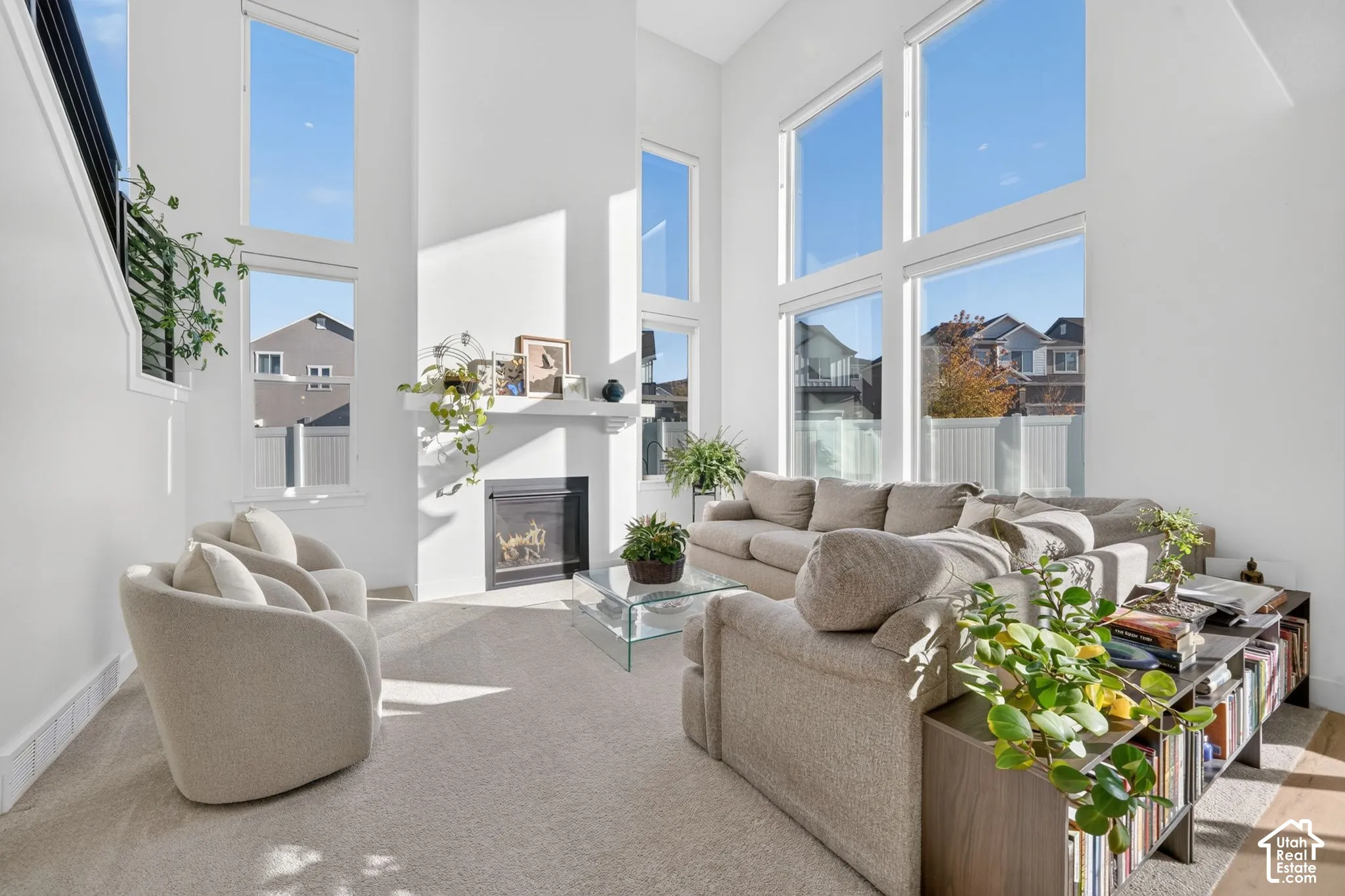 Double-height ceilings, floor-to-ceiling windows, wall-mounted fireplace with mantel, and staircase with black metal railing