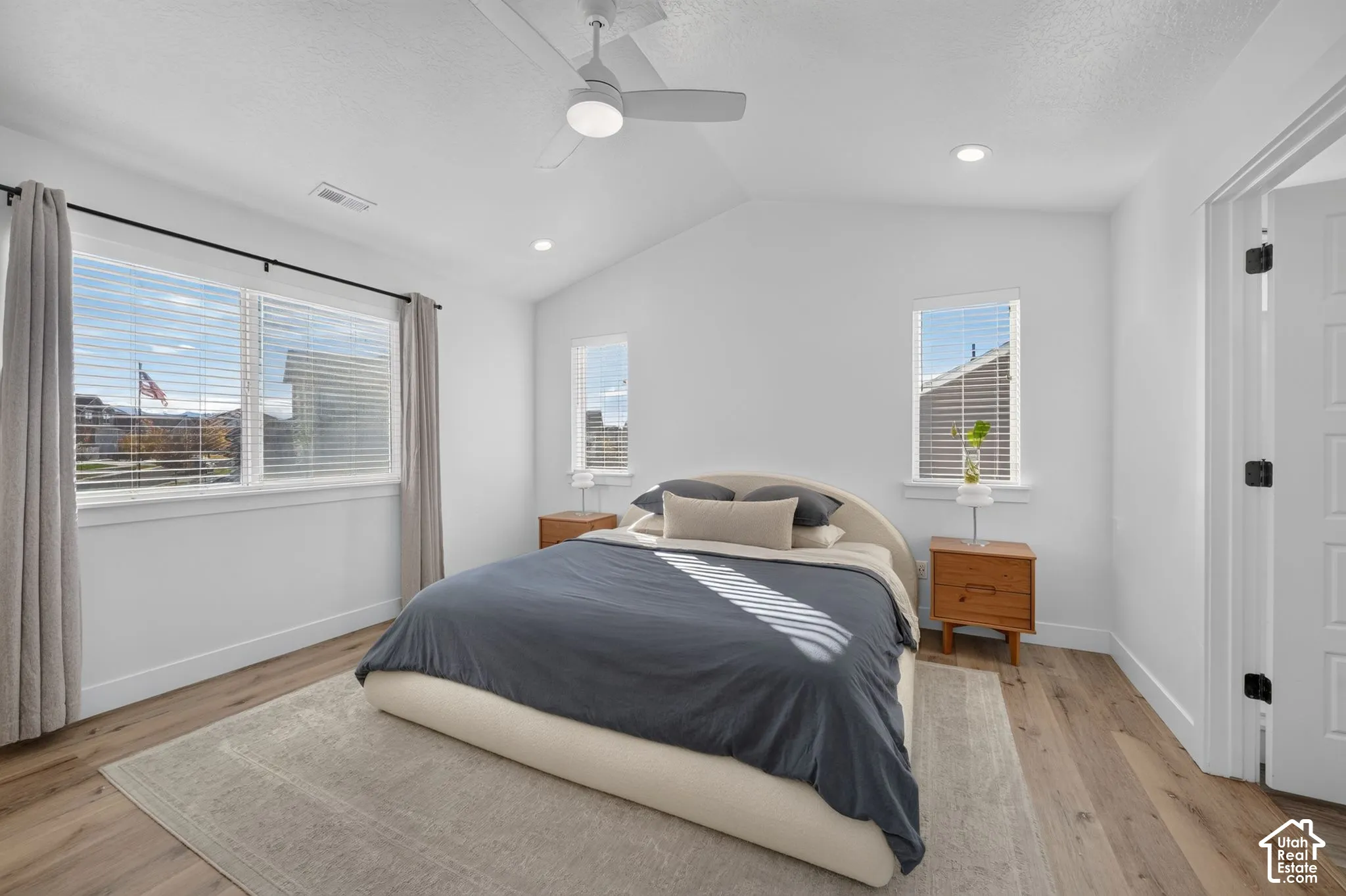 Vaulted ceilings, wood-finish flooring, recessed lighting, and a neutral color palette with multiple windows