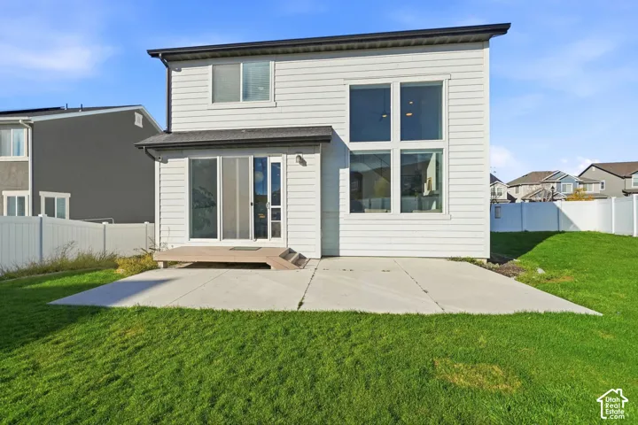 Rear exterior featuring horizontal lap siding, large dual-pane windows, a concrete patio, a composite deck, and white vinyl perimeter fencing