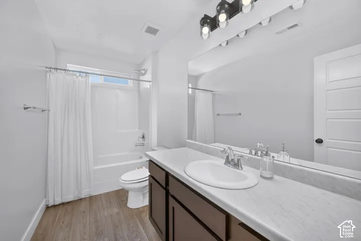 Bathroom featuring a wood-finish floor, a vanity with a stone-composite countertop and integrated oval sink, a full-width mirror, a three-light fixture, and a tub-shower combination with an enclosure
