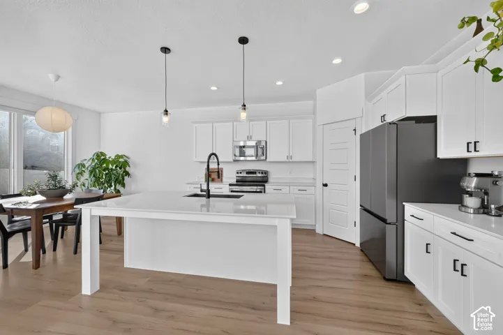 Kitchen featuring white shaker-style cabinetry, quartz-surface center island with an undermount sink, stainless steel appliances, wood-finish flooring, and recessed lighting