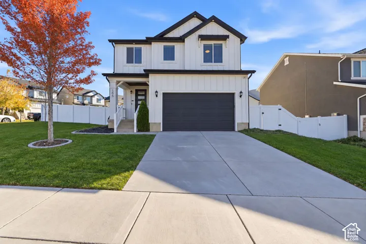 Two-story residence featuring white vertical siding, a front-facing attached garage, a covered entryway, and white perimeter fencing