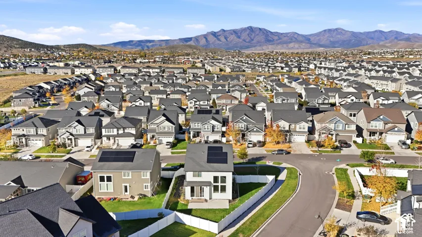 Aerial perspective featuring a two-story residence with rooftop solar panels, a fenced backyard, and mountain backdrops