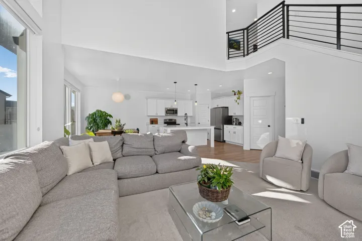 Open-concept interior featuring double-height ceilings, a kitchen with white cabinetry and a central island, recessed lighting, and a metal horizontal-bar staircase railing