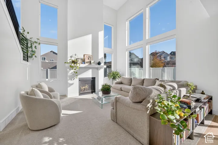 Double-height ceilings, floor-to-ceiling windows, wall-mounted fireplace with mantel, and staircase with black metal railing