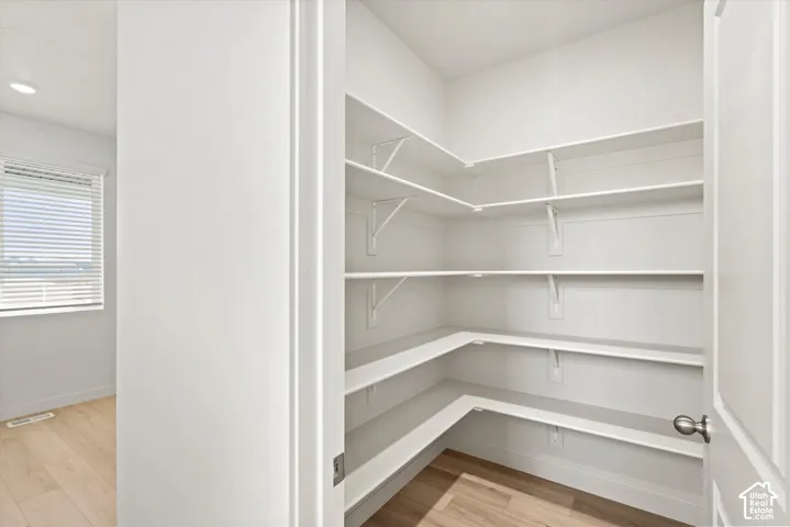 Walk-in storage pantry featuring white tiered shelving and wood-finish flooring