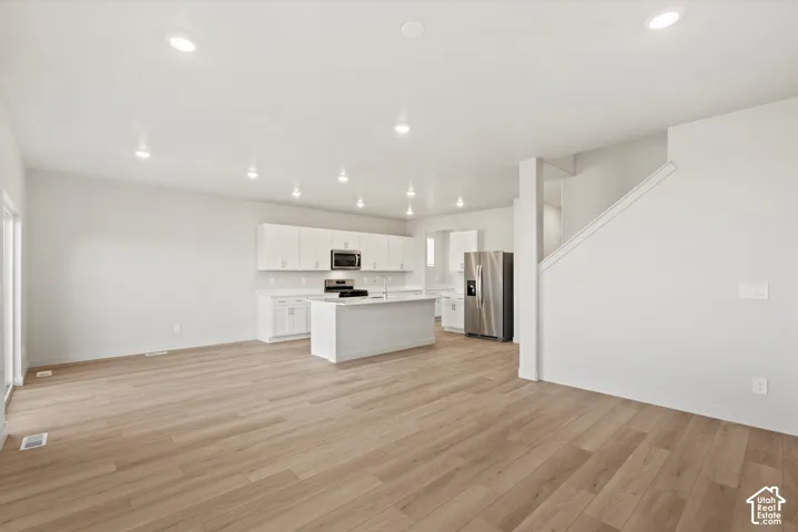 Open-concept interior featuring wood-finish flooring, recessed lighting, white cabinetry, a central kitchen island, and stainless steel appliances