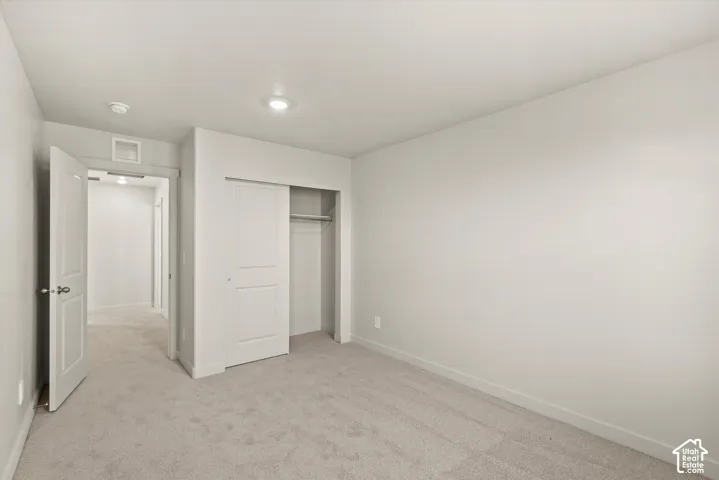 Neutral-toned interior space featuring wall-to-wall carpeting, recessed ceiling lighting, a built-in closet with sliding panel doors, and solid-core interior doors