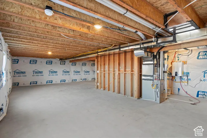 Unfinished lower level featuring exposed wood joist ceilings, concrete flooring, exposed wall studs, an integrated HVAC system, and a tankless water heater
