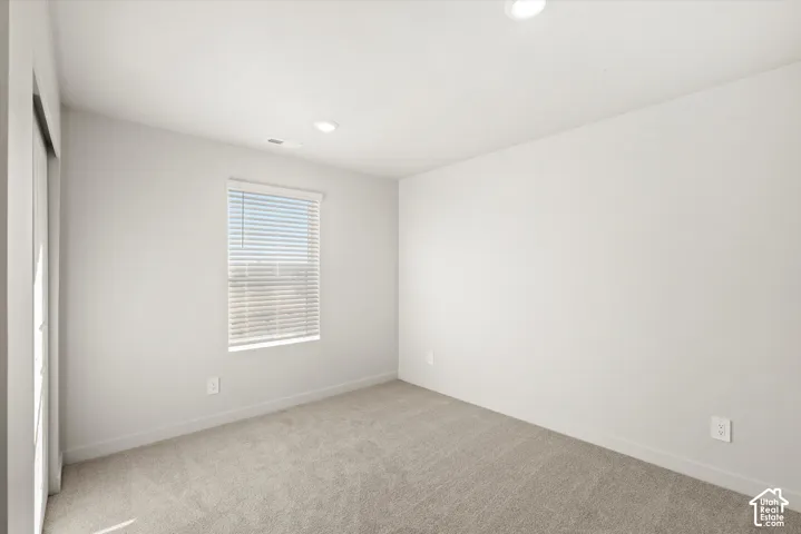 Neutral-toned interior space featuring recessed ceiling lighting, wall-to-wall carpeting, and a single window with horizontal blinds