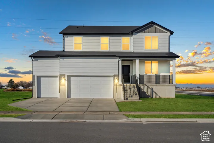 Two-story residence featuring horizontal siding, a multi-car garage, covered front porch with metal railing, and concrete driveway