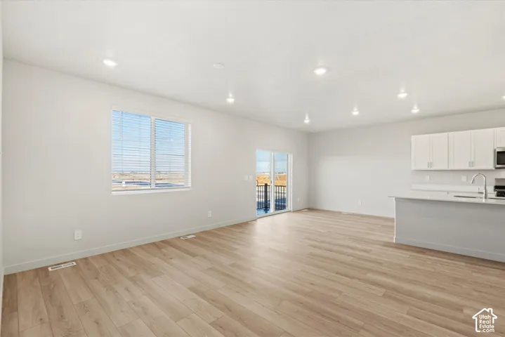 Open-concept interior featuring wood-finish flooring, recessed lighting, white cabinetry, and a kitchen island with a neutral countertop