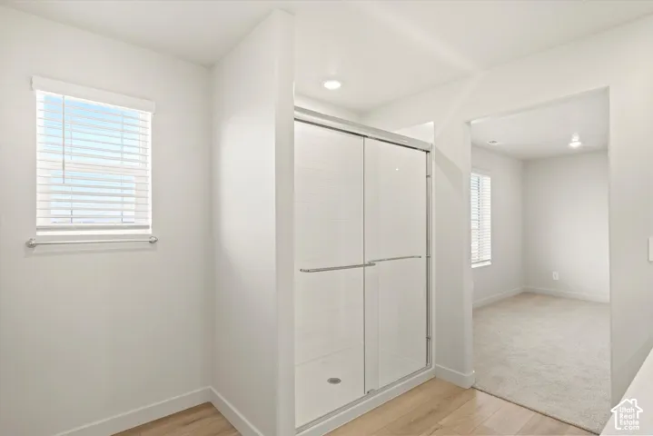 Walk-in shower featuring a glass enclosure with metallic hardware, recessed ceiling lighting, light wood-finish flooring, and horizontal blind window treatments