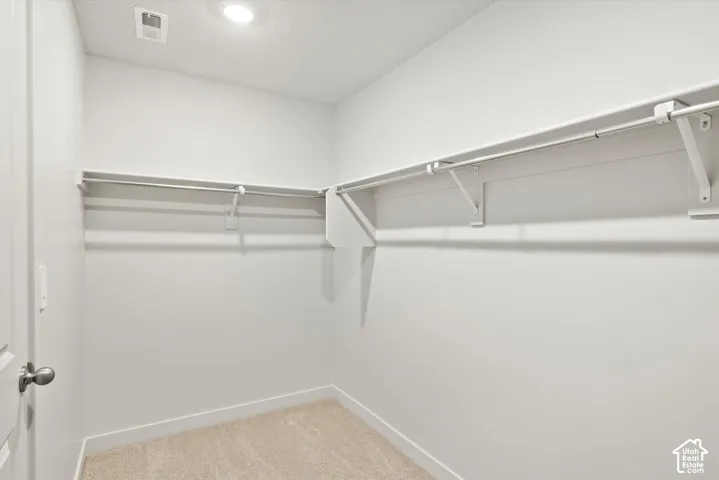 Walk-in closet featuring neutral carpeting, white interior walls, recessed lighting, and wrap-around white shelving with integrated hanging rods
