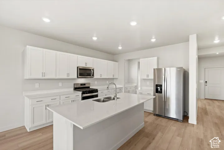 Kitchen featuring white shaker-style cabinetry, quartz countertops, a central island with a double-basin stainless steel sink, stainless steel appliances, and wood-finish flooring