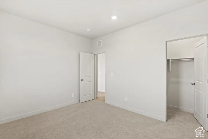 Neutral-toned wall-to-wall carpeting, recessed ceiling lighting, and a walk-in closet featuring built-in shelving