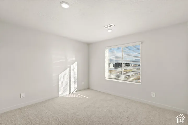 Neutral-toned room featuring wall-to-wall carpeting, recessed ceiling lighting, and a window with horizontal blinds