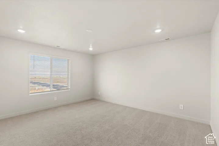 Neutral-toned room featuring wall-to-wall carpeting, recessed ceiling lighting, and a window with horizontal blinds