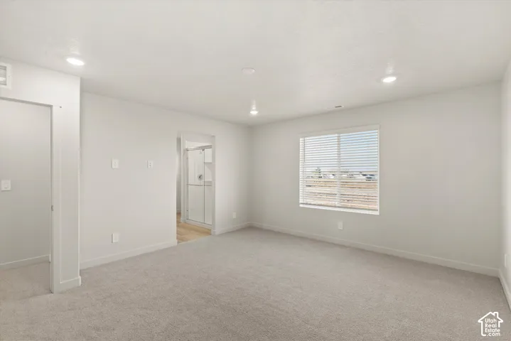 Neutral-toned carpeted room featuring recessed lighting, a single-pane window with horizontal blinds, and a doorway revealing a tiled-floor bathroom