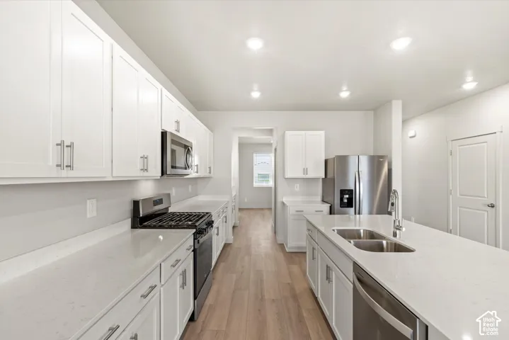 Kitchen featuring white cabinetry, solid-surface countertops, wood-finish flooring, stainless steel appliances, and a central island with an integrated dual-basin sink