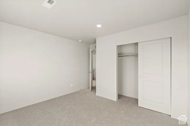 Neutral-toned wall paint, recessed lighting, carpeted flooring, and a closet featuring a sliding panel door