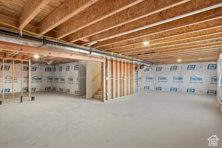 Unfinished basement featuring exposed wood joists, concrete flooring, stud-framed walls, and vapor barrier insulation