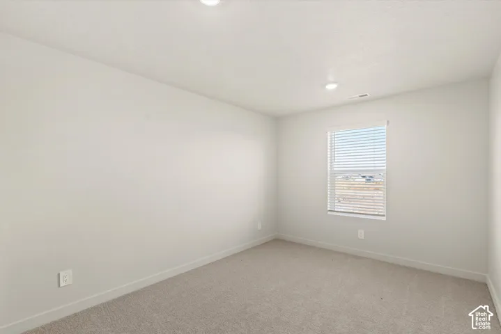 Neutral-toned interior space featuring light-colored wall paint, plush carpeting, recessed lighting, and a window with horizontal blinds