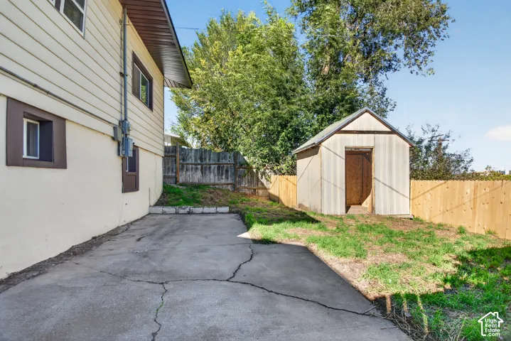 Exterior yard space featuring a concrete patio, detached storage structure, and wood-panel fencing
