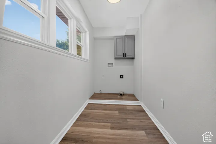 Utility space featuring wood-finish flooring, multi-pane windows, wall-mounted grey cabinetry, and integrated plumbing and electrical hookups