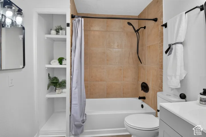 Bathroom featuring built-in recessed shelving, a white tub and shower surround with tan tile, a matte black shower fixture, and a vanity with a white countertop