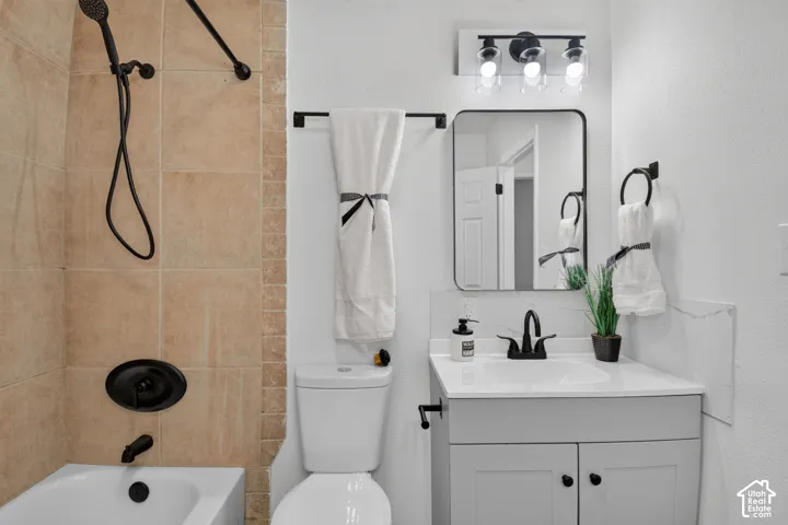 Bathroom featuring light-toned tile shower surround with matte black plumbing fixtures, vanity with solid surface countertop, rectangular mirror with black metal frame, and three-light vanity fixture with clear glass shades