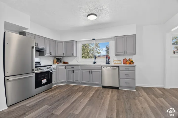 Kitchen featuring grey shaker-style cabinetry, stainless steel appliances, white solid-surface countertops with veining, and wood-finish flooring